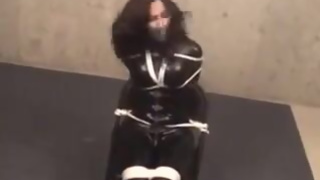 Girl in black latex catsuit tied to chair and tape-gagged