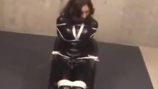 Girl in black latex catsuit tied to chair and tape-gagged