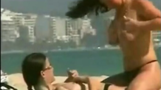 Two lesbians oil each other topless at the beach